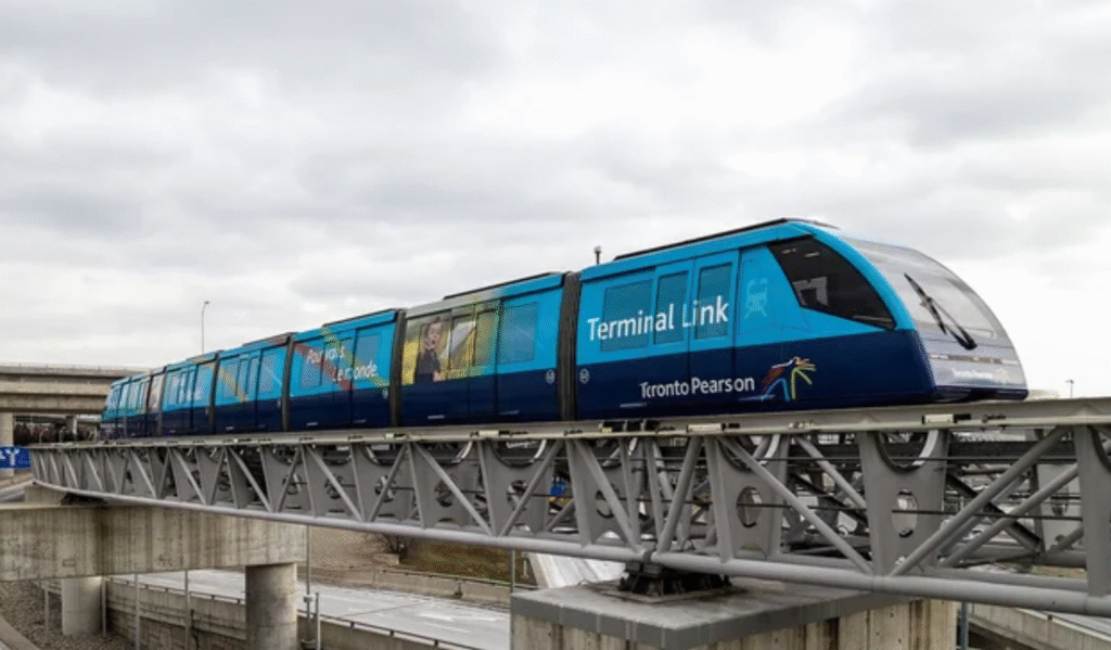 A modern, blue and black Toronto Pearson Terminal Link train, adorned with "Terminal Link" and "Toronto Pearson" branding, travels on an elevated track against a cloudy sky.